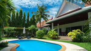 Ein Pool mit gewölbter Kante, umgeben von einem gepflegten Rasen und verschiedenen tropischen Pflanzen.