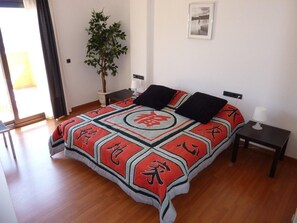 A bedroom with a bed, a nightstand, a lamp, a potted plant, and a framed picture on the wall.