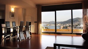 Ein modernes Hotelzimmer mit einem großen Panoramafenster, einer Essecke mit Tisch und Stühlen und Blick auf eine Küstenstadt.