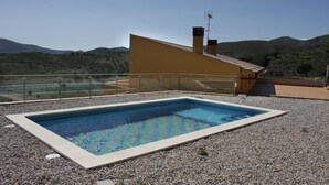 Ein rechteckiger Swimmingpool mit einer klaren, blauen Wasseroberfläche, umgeben von einem Kiesgrund, mit einem gelben Gebäude mit geneigtem Dach im Hintergrund.