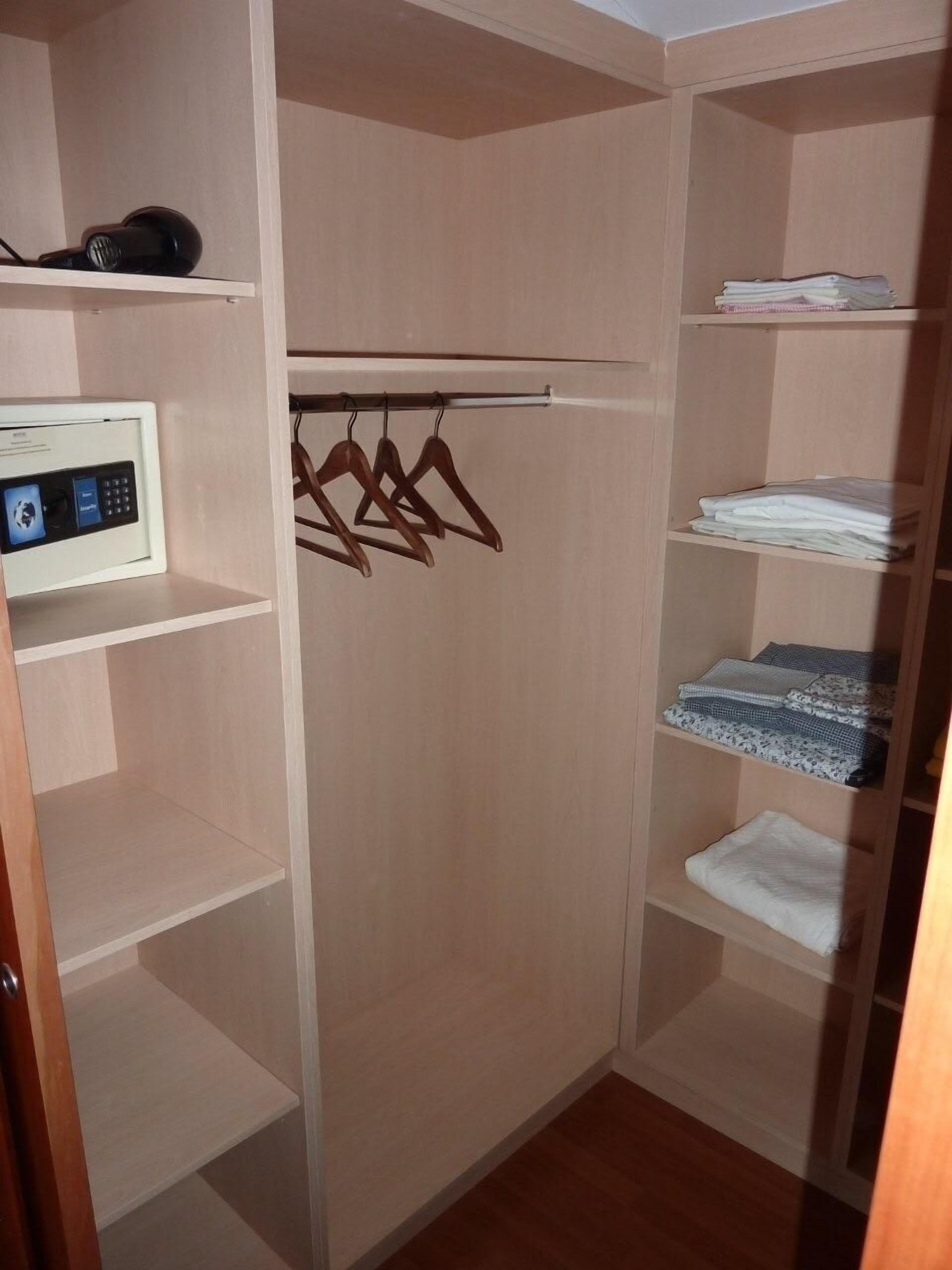 A walk-in closet with wooden shelves, a hanging rod, and a microwave on the left.