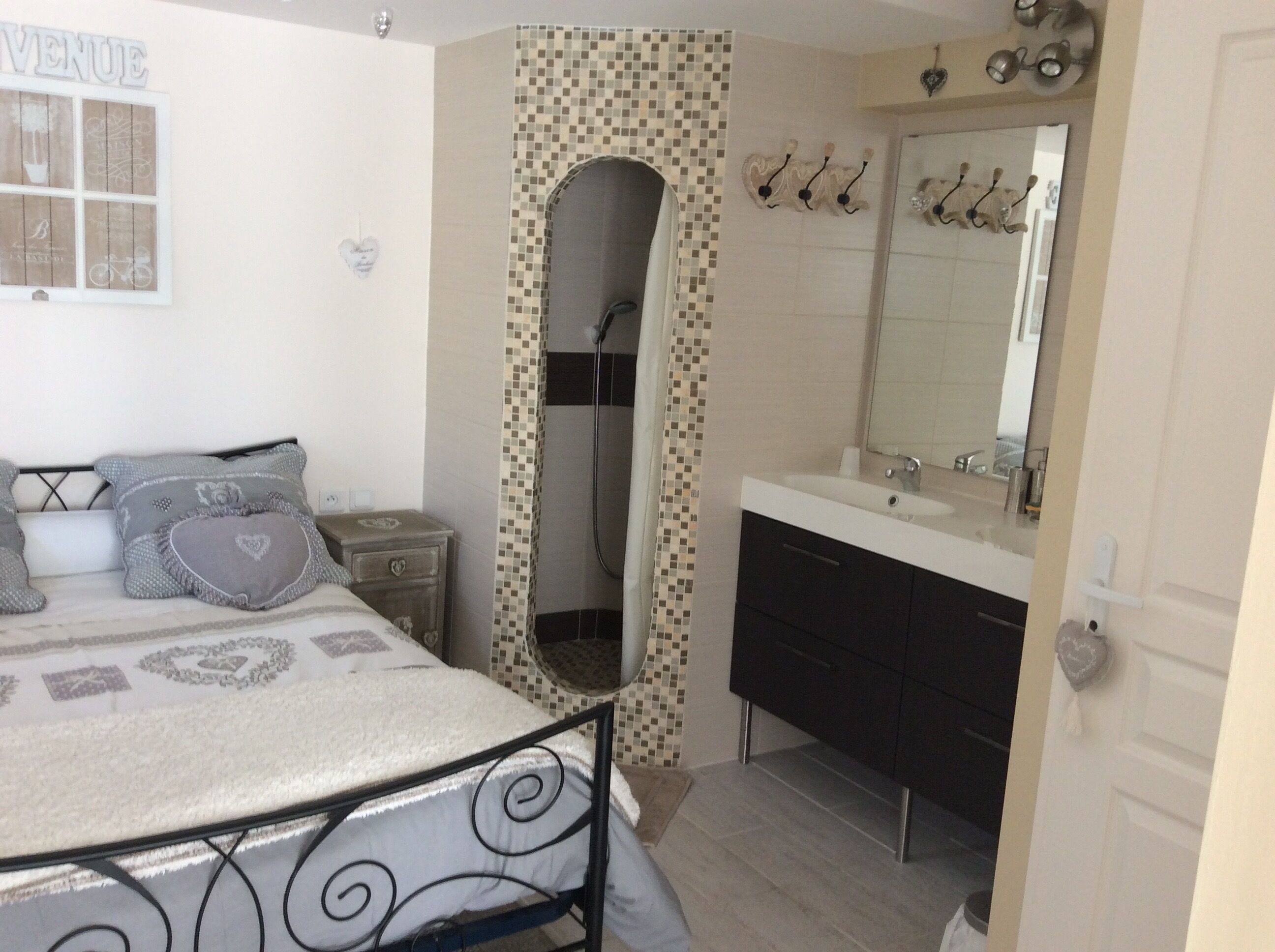 A bedroom with a bed, a nightstand, a bathroom with a sink and mirror, and a shower area.