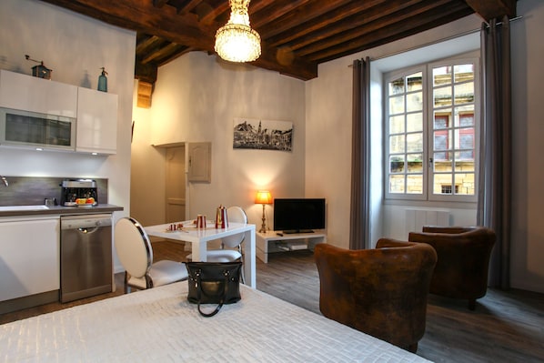 Een moderne keuken met een vaatwasser, een eettafel met stoelen, een televisie en een raam met gordijnen.