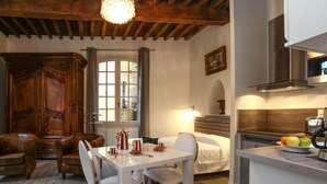 Une pièce confortable comprenant une table à manger, des chaises, un buffet en bois, une fenêtre avec des rideaux, un lit et un coin cuisine.