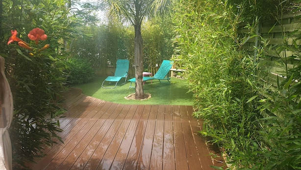 A wooden deck with artificial grass, two blue chairs, and a tree. - Very nice little villa at the Franqui  (Leucate)