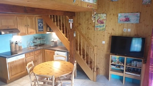 A kitchen with wooden cabinets, a dining table with chairs, a wooden staircase, and a television on a wooden stand. - Very nice little villa at the Franqui  (Leucate)