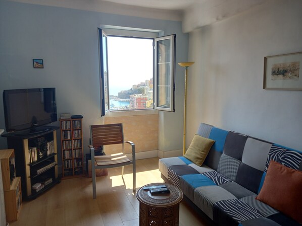 A living room with a TV, bookshelf, chair, sofa, and a window with a view.