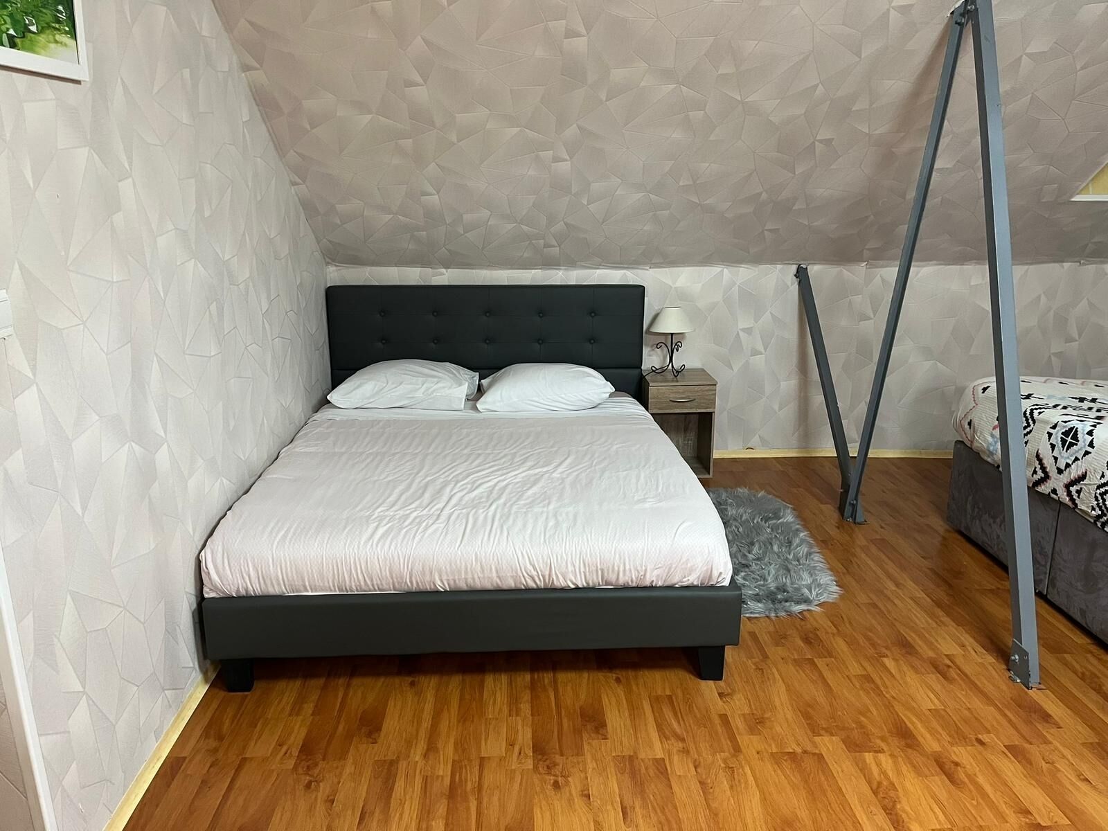A bedroom with a bed, a nightstand, a lamp, a gray furry rug, and a canopy bed frame.