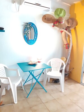 A room with a blue table, white chairs, a decorative wall piece, and a rustic wooden structure. - STUDIO LES PIEDS DANS L'EAU FACE AU LAGON.<br>50m from the beach. des Alizés (Le Moule)