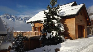 A wooden cabin with a snow-covered roof, surrounded by snow and a mountain backdrop. - Chalet Jonquille - 12 persons with outdoor Jacuzzi, 6 bedrooms (Oz)