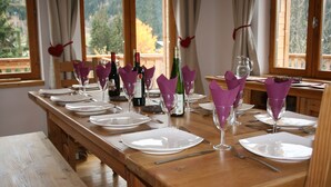 A dining table set with plates, glasses, and wine bottles, with a view of trees through the window. - Chalet Jonquille - 12 persons with outdoor Jacuzzi, 6 bedrooms (Oz)
