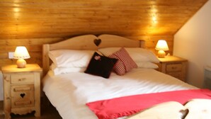 A bedroom with a wooden ceiling, a bed with white bedding, a red throw blanket, and two bedside lamps. - Chalet Jonquille - 12 persons with outdoor Jacuzzi, 6 bedrooms (Oz)