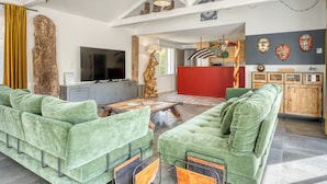 Uma sala de estar espaçosa com sofás estofados em verde, uma mesa de centro de madeira, uma parede em destaque vermelha e uma televisão de tela plana grande.