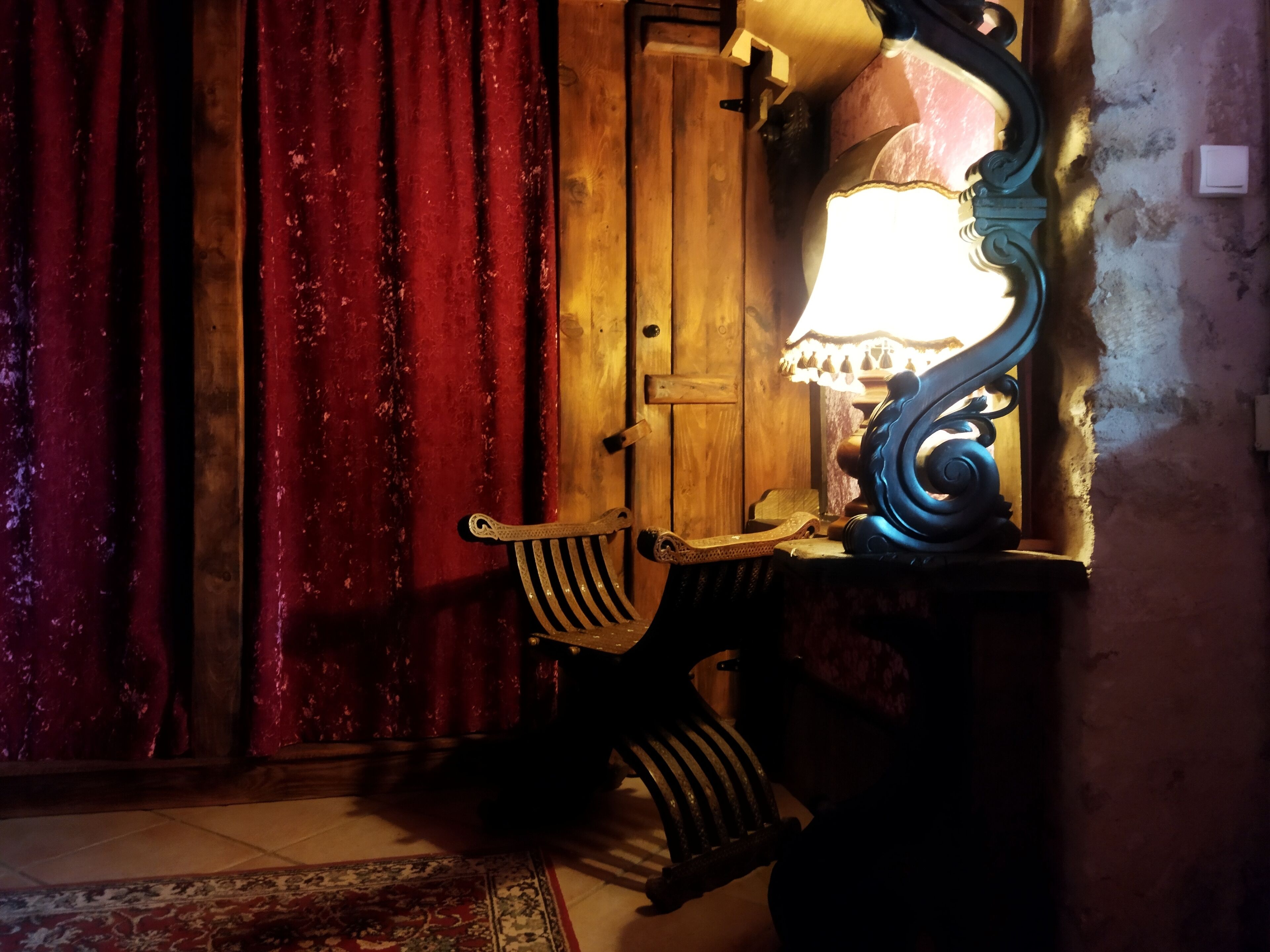 A room with a wooden door, a lamp on a table, and a patterned rug on the floor.