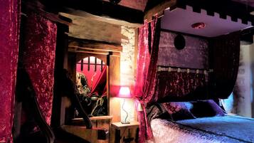 A medieval-themed room with a bed, a small table, and a red curtain.