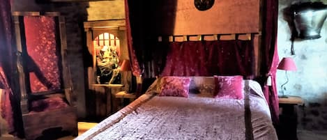 A medieval-themed bedroom with a four-poster bed, a stone wall with a shield emblem, and a small table with a lamp.