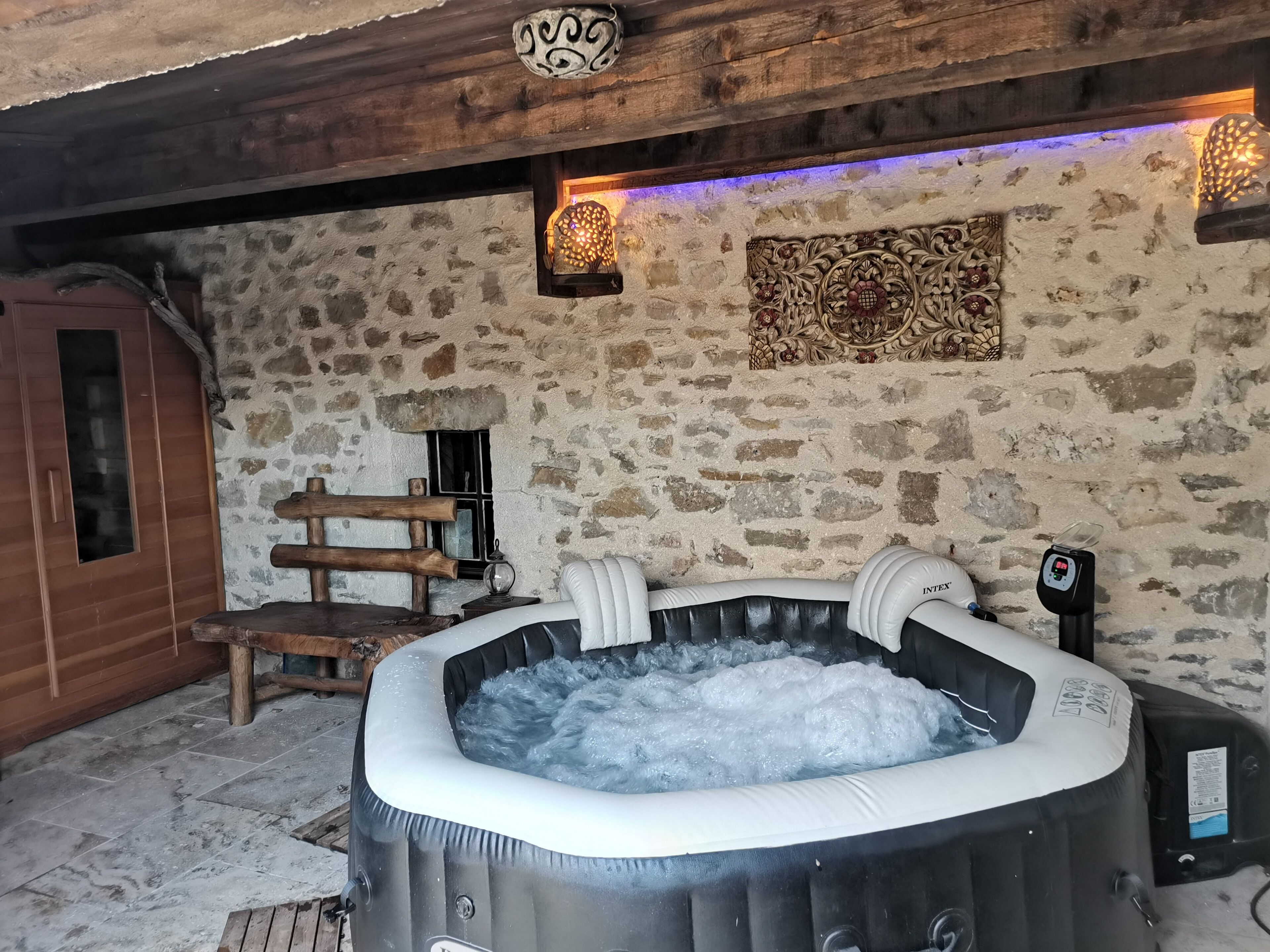 Una habitación con paredes de piedra, un banco de madera, un armario de madera y una bañera de hidromasaje con agua.