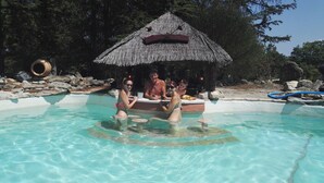 Zona de piscina con agua cristalina, una estructura de techo de paja y una costa rocosa.