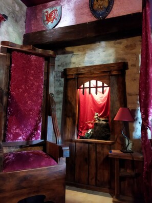 Une pièce rustique avec une porte en bois, un rideau rouge, un banc en bois et une petite table avec une lampe.