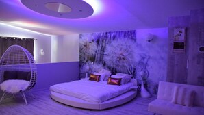 A modern bedroom with a round bed, a hanging chair, and a white sofa.