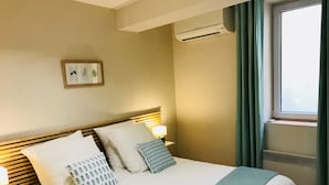A neatly made bed with white linens and a blue throw, a bedside lamp, and a framed picture on the wall. - Quiet, air-conditioned apartment for 4 in city center (Cassis)