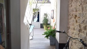 A narrow hallway with a bicycle parked on the right, leading to a wooden deck with potted plants. - IDEAL COZY HOUSE FOR 1 COUPLE AND 2 CHILDREN  (Sainte-Marie-de-Ré)