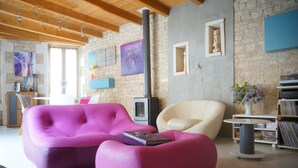 A modern living room with a stone wall, a fireplace, a pink sofa, a white armchair, and a bookshelf. - IDEAL COZY HOUSE FOR 1 COUPLE AND 2 CHILDREN  (Sainte-Marie-de-Ré)