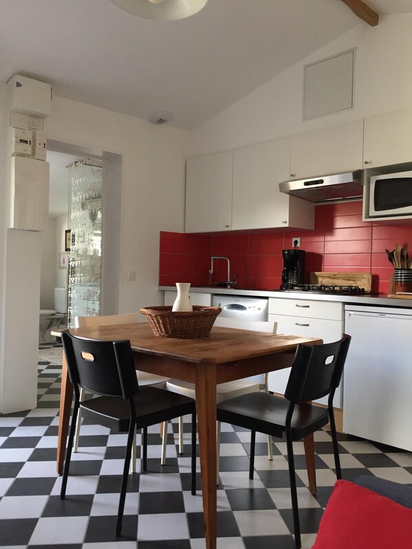 Een keuken met een zwart-wit geruite vloer, een eettafel met stoelen, een magnetron en een Bosch vaatwasser.