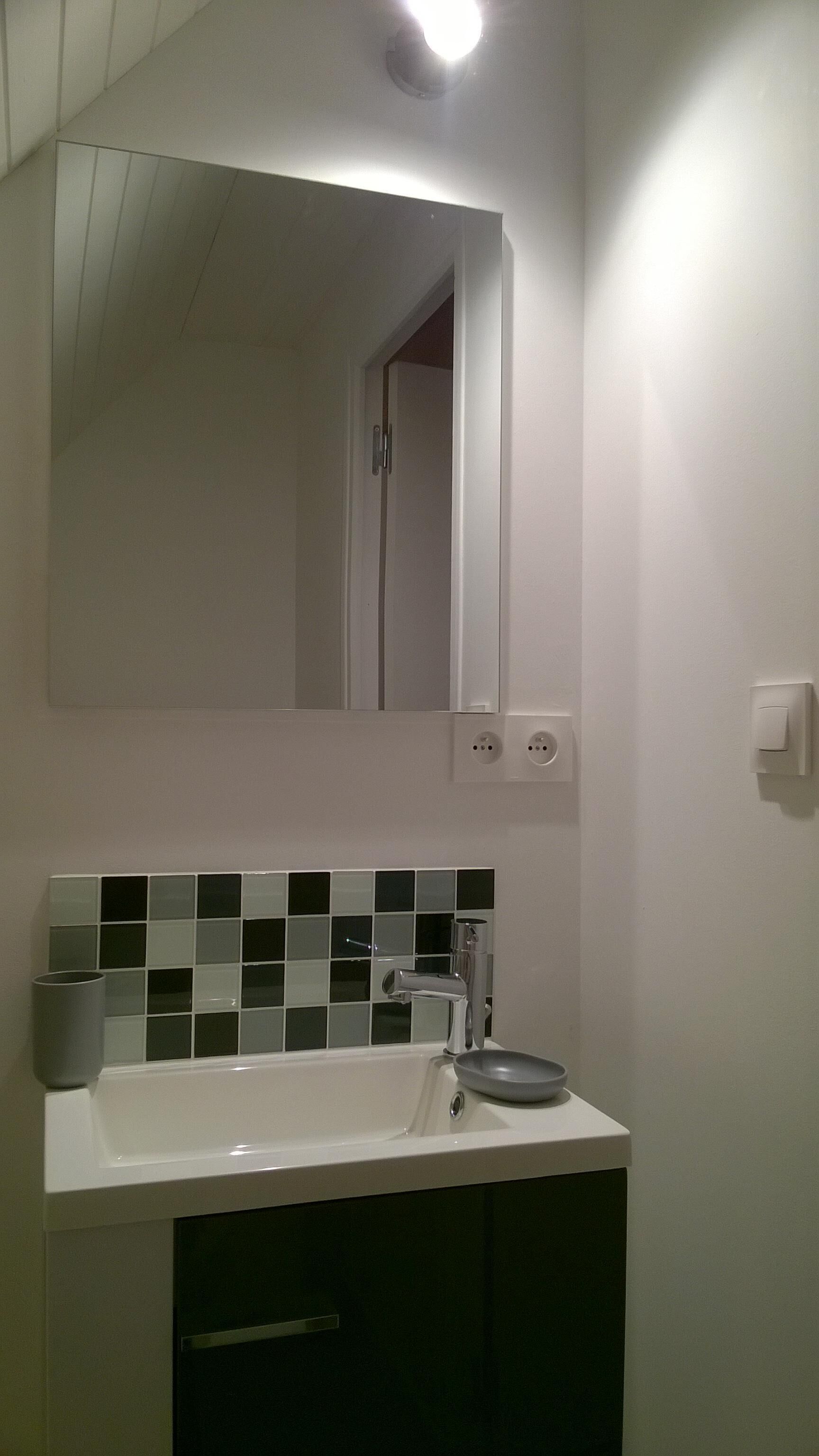 Un baño con un lavamanos blanco, un espejo y un salpicadero de azulejos.
