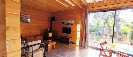 Acogedor interior de cabaña de madera con chimenea, televisor y comedor con sillas rojas.