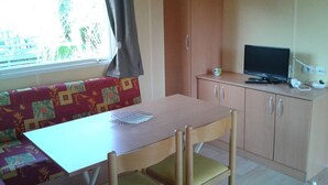 A compact room with a wooden table, a single chair, a sofa, and a television on a cabinet.