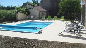 A swimming pool with a blue cover, surrounded by lounge chairs and a small building in the background. - house high capacity with private pool (Meursanges)