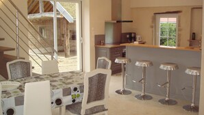 A dining area with a table set for four, a kitchen with a window, and a staircase leading to an upper level. - house high capacity with private pool (Meursanges)