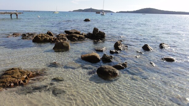 A coastal scene with clear water, rocks, and distant boats.
