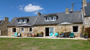 Une maison en pierre dotée d’un patio aménagé avec des sièges d’extérieur et un parasol.