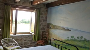Une chambre à coucher avec un lit, une chaise, une fenêtre avec des rideaux et une fresque murale.