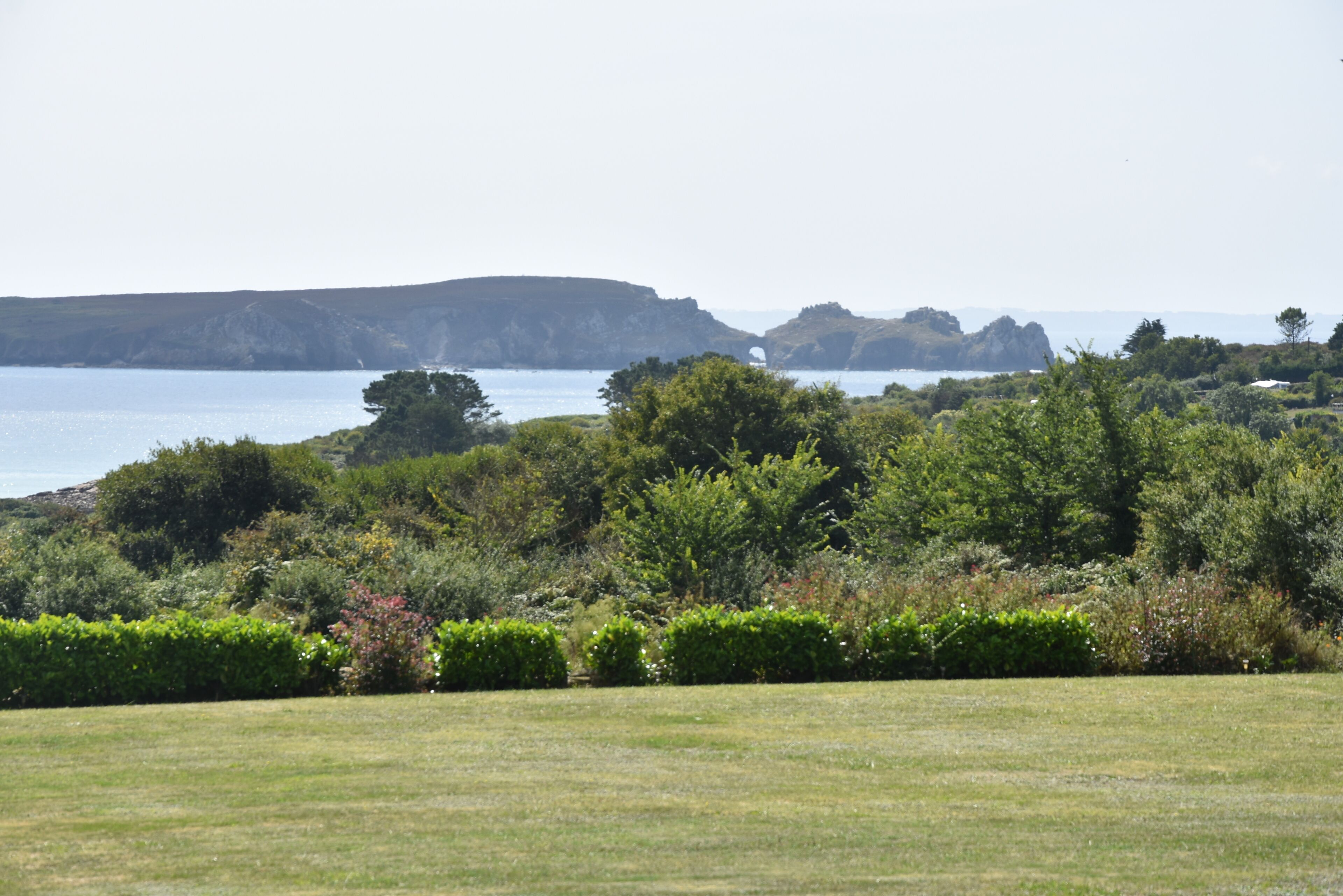 Un paysage côtier avec une prairie, une végétation arbustive dense et des falaises rocheuses en arrière-plan.