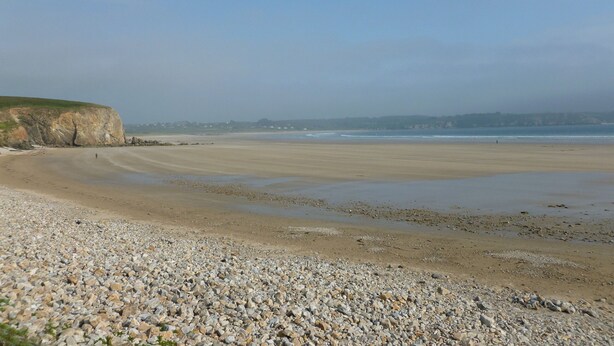 Une plage de galets, avec une falaise et l’océan en arrière-plan.