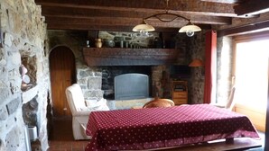 Une pièce rustique avec un mur en pierre, un plafond en bois, une cheminée, un lit recouvert d’une courtepointe à pois, une table en bois et une chaise.