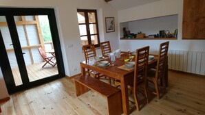 A dining area with a wooden table set for four, surrounded by chairs, with a bench at the end. A door leads to an outdoor area with a chair. - GITE DE LA TOUR * * * *, SPA DETENTE MASSAGE 3 rooms with individual bathrooms (Langatte)