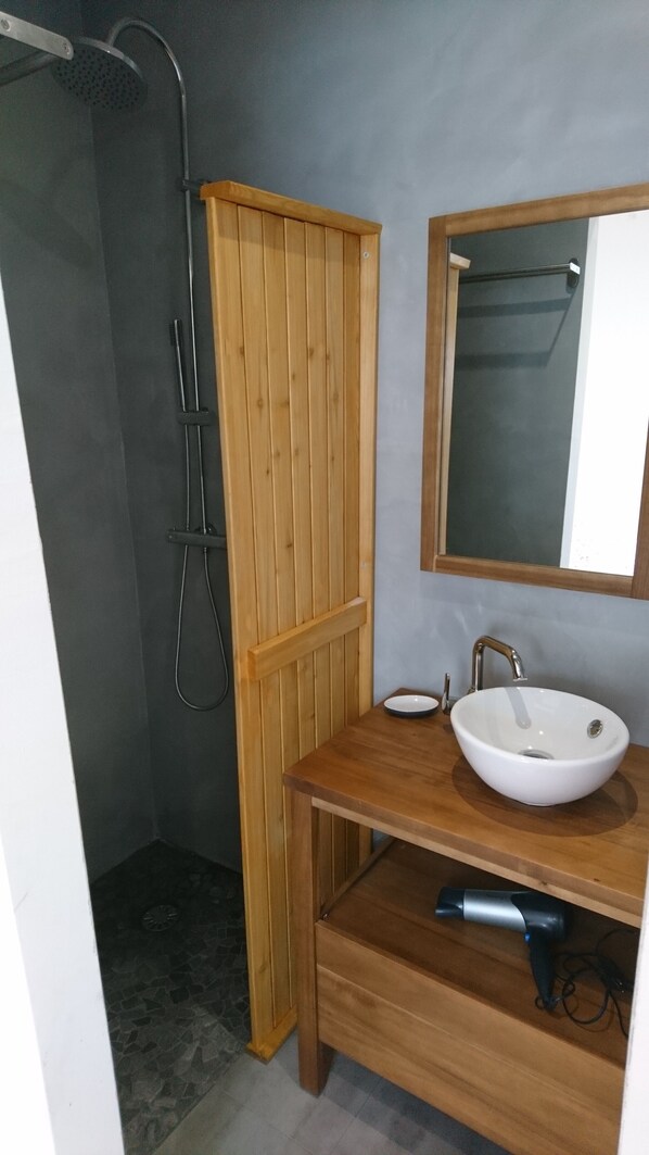 Een badkamer met een houten wastafelmeubel, een witte wasbak, een spiegel en een douchehoek.