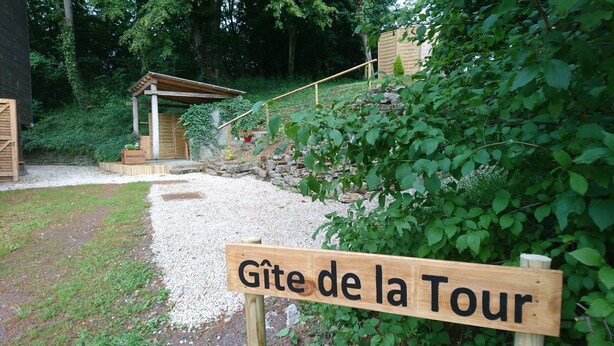 A wooden sign reading "Gîte de la Tour" in a garden setting with a gravel path, wooden structures, and greenery. - GITE DE LA TOUR * * * *, SPA DETENTE MASSAGE 3 rooms with individual bathrooms (Langatte)