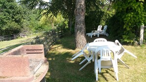 An outdoor seating area with white plastic chairs and a table, surrounded by a stone wall and trees. - Four independent cottages in an old farmhouse with swimming pool - "Loire" (Limbrassac)