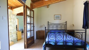 A bedroom with a bed, a wooden dresser, a nightstand, a stone wall, and a door leading to another room. - Four independent cottages in an old farmhouse with swimming pool - "Loire" (Limbrassac)