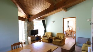 A cozy room with a wooden ceiling, a stone wall, a flat-screen TV, two armchairs, a dining table, and a small kitchen area. - Four independent cottages in an old farmhouse with swimming pool - "Loire" (Limbrassac)
