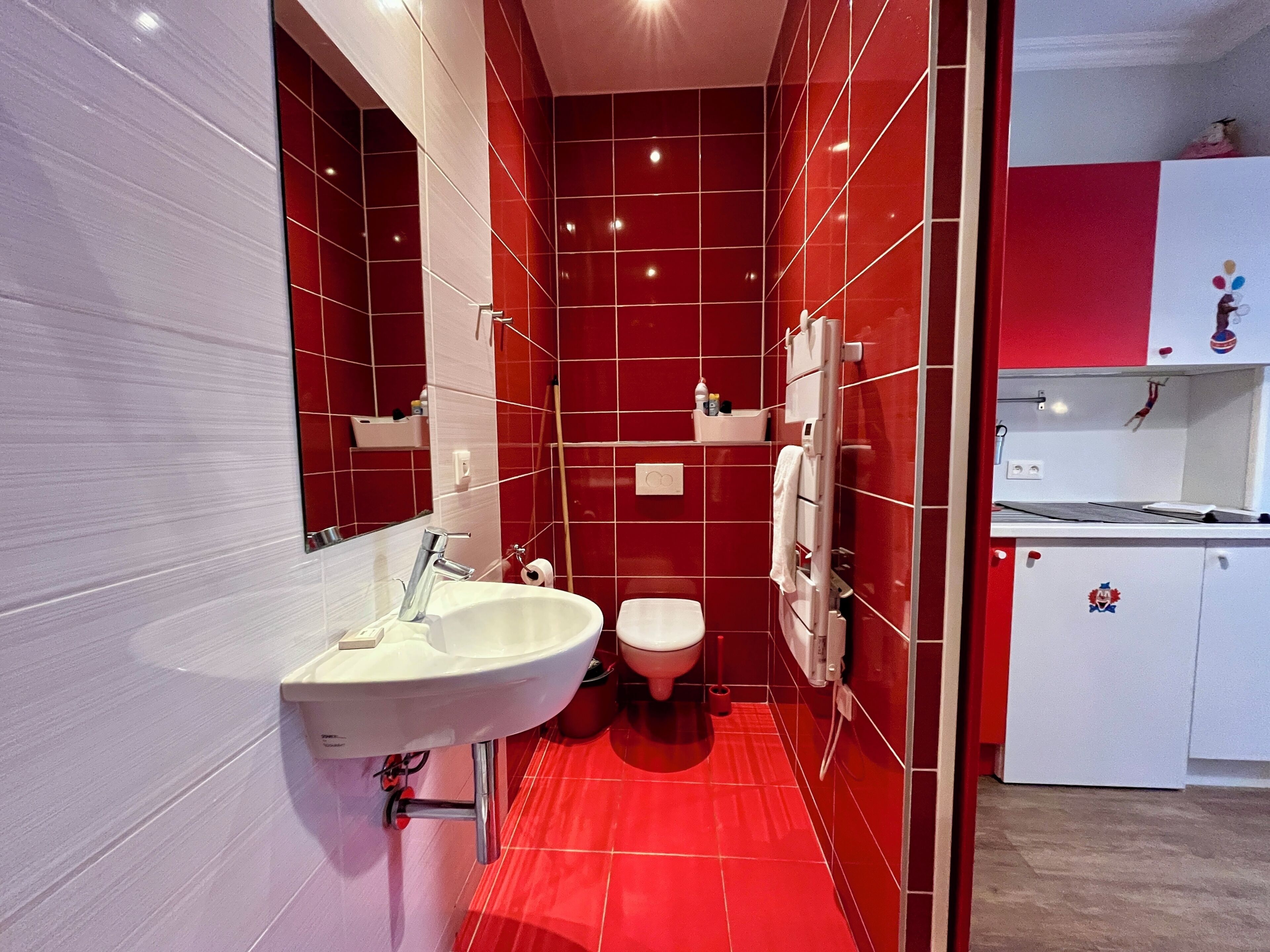 A modern bathroom with a white sink, a toilet, and a red-tiled wall.