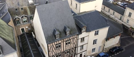 A traditional half-timbered building with a steeply pitched roof, adjacent to a body of water and a parking area with several cars.