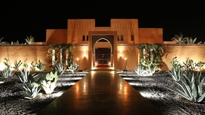 A building with a central archway, surrounded by cacti and illuminated by wall-mounted lights. - Premium Suite for 2 in Marrakesh (Marrakech)