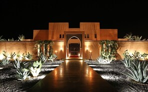 A building with a central archway, surrounded by cacti and illuminated by wall-mounted lights. - Premium Suite for 2 in Marrakesh (Marrakech)