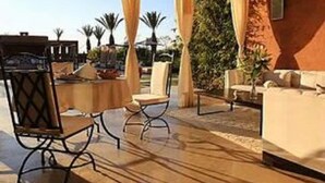 An outdoor patio area with a round table and chairs, a red building, and palm trees in the background. - Premium Suite for 2 in Marrakesh (Marrakech)